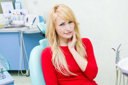 Patient in dental chair holding jaw before appointment at  Dental Care of Burlington in Burlington, MA