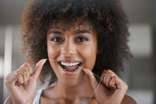 Beautiful Black woman flossing before appointment at Dental Care of Burlington in Burlington, MA