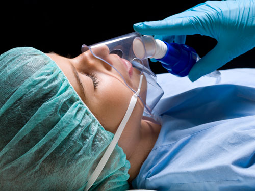 gloved hand holds breathing mask to sedated patient's face