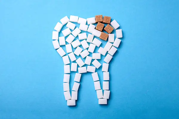 A tooth shape made of sugar cubes with brown sugar cubes at the top, illustrating tooth decay.